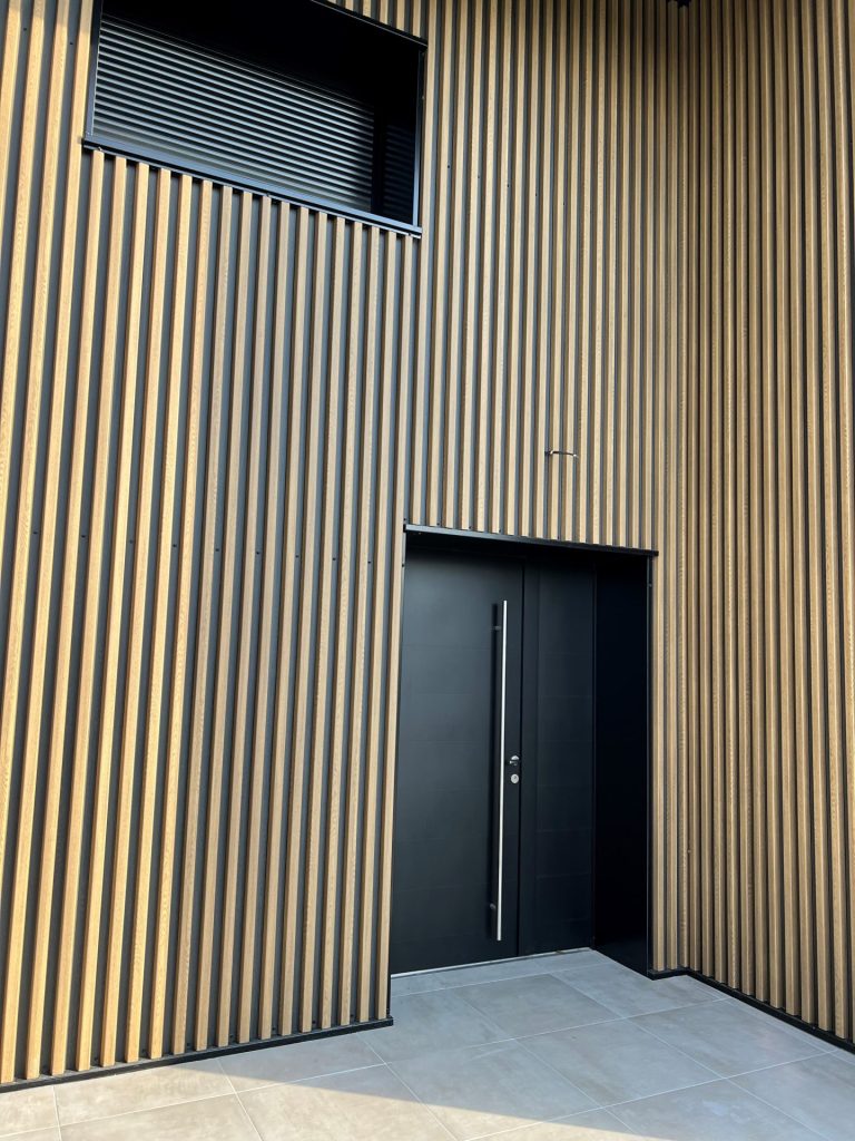 Porte d'entrée aluminium noire sur façade en bardage bois